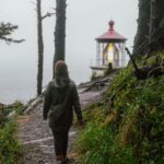 Woman in Green Jacket Walking on Pathway Near Body of Water