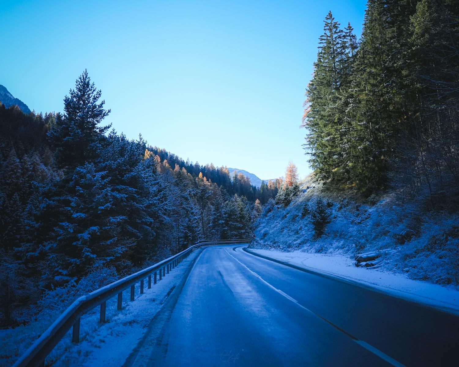 Road Trip Scenic Winter  A serene winter road winding through snow-covered mountain forest at sunrise.